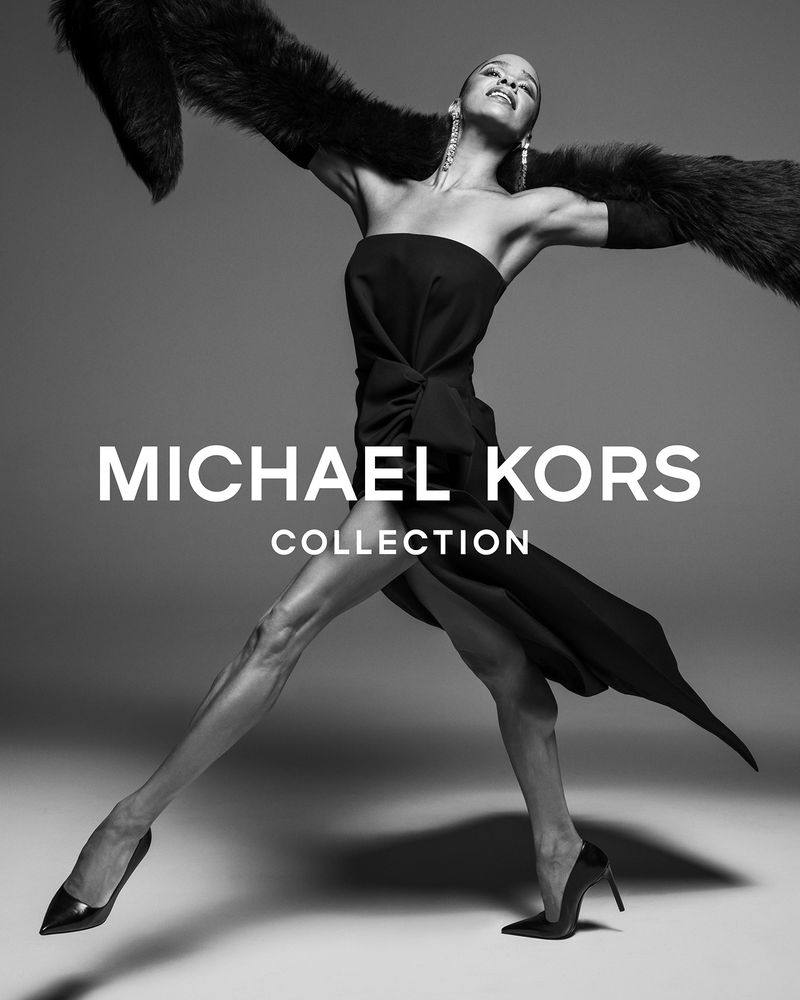 A model in a strapless black dress with a fur stole strikes a dynamic pose, wearing long opera gloves and high heels in a studio.