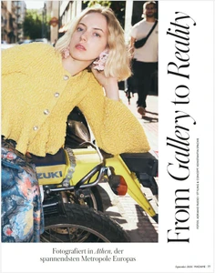Model Sylwia Kuta wearing a textured yellow cardigan and pink earrings seated on a yellow motorcycle on a sunlit city street.