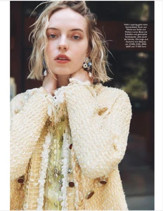 Blonde woman wearing a textured cream tweed jacket and ornate drop earrings with her hands behind her neck.
