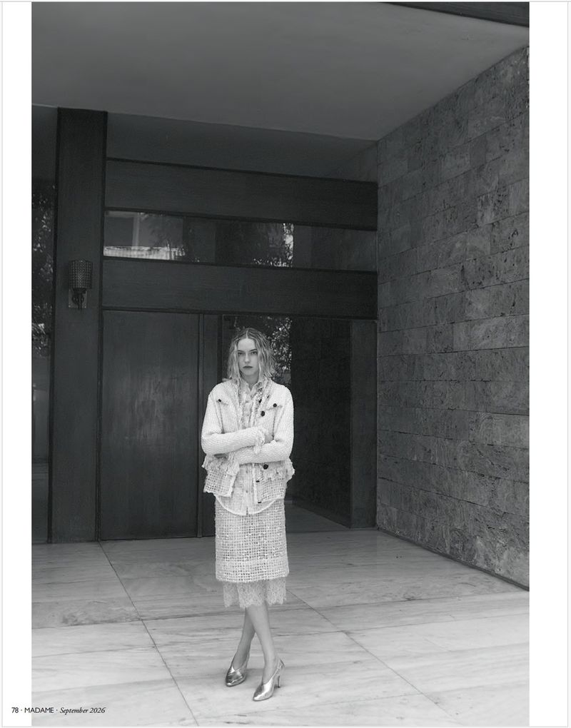 Model Sylwia Kuta posing in a textured layered jacket and skirt on a tiled patio by a stone block wall in black and white.