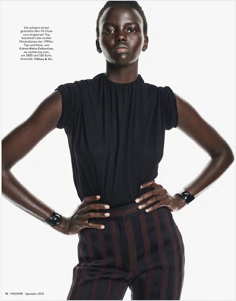 Model Ajak Dhieu wearing a black sleeveless top, pinstriped trousers, and black cuff bracelets against a white background.