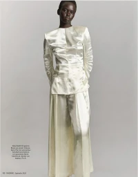 Ajak Dhieu standing in a cream draped satin blouse and matching wide-leg trousers against a soft grey studio background.