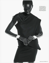 Model Ajak Dhieu wearing a draped black sleeveless dress with white wrist cuffs against a seamless white studio background.