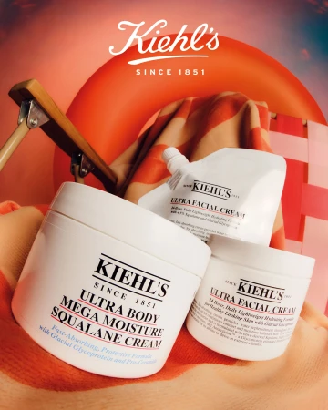 Kiehl's skincare product promotion featuring three containers of cream against an orange striped beach towel and an inflatable ring.