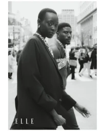 Monochrome fashion portrait of a Black woman and man walking along a busy city street in tailored blazers.