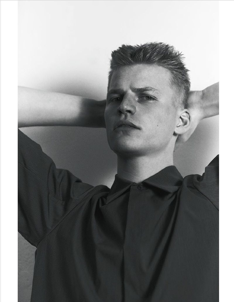 Monochrome portrait of model Timo Pan wearing a dark collared shirt with hands behind his head against a light backdrop.