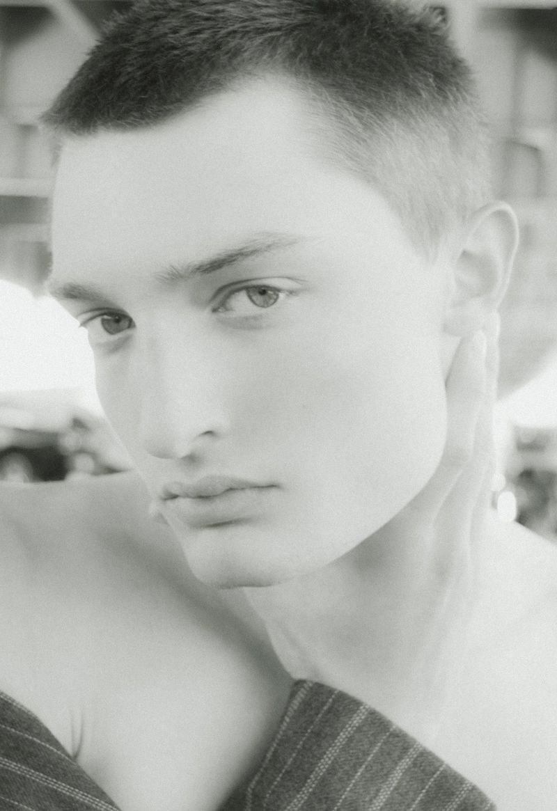 Black and white close-up portrait of a young man with short hair resting his hand against his neck.