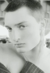 Black and white close-up portrait of a young man with short hair resting his hand against his neck.
