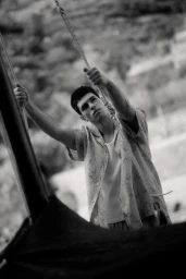 Model Denis Jovanovic holding ropes and wearing a patterned short-sleeve shirt in a black and white fashion portrait.