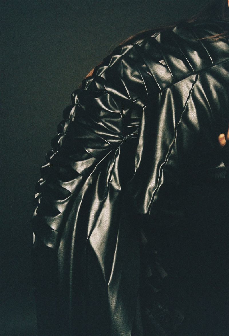 Close-up fashion shot of a black quilted leather jacket featuring a tailored silhouette and textured design, set against a dark background.