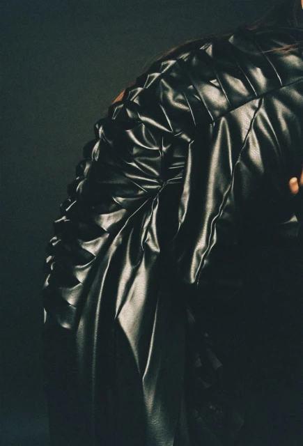 Close-up fashion shot of a black quilted leather jacket featuring a tailored silhouette and textured design, set against a dark background.