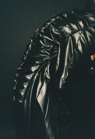 Close-up fashion shot of a black quilted leather jacket featuring a tailored silhouette and textured design, set against a dark background.