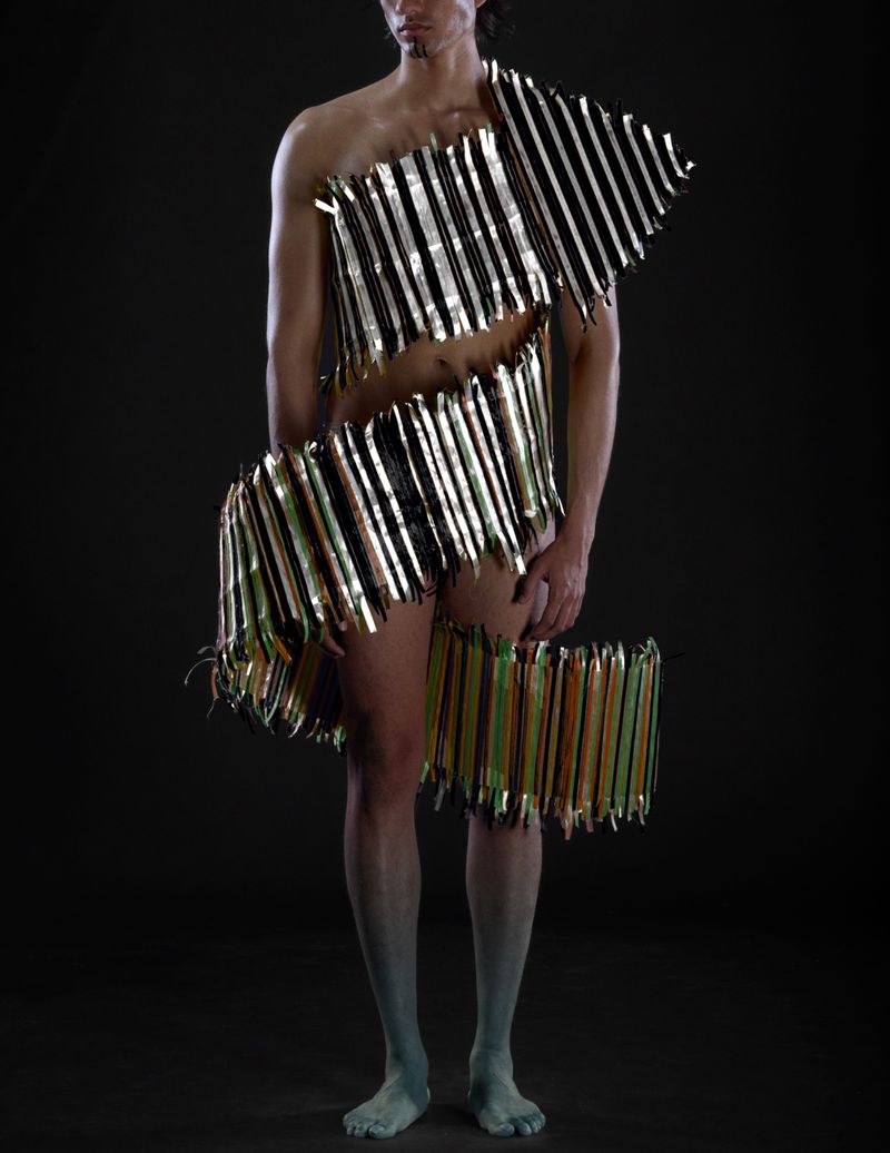 Man in metallic striped avant-garde fashion, posing in a full shot against a dark backdrop, creating a dramatic and artistic visual.
