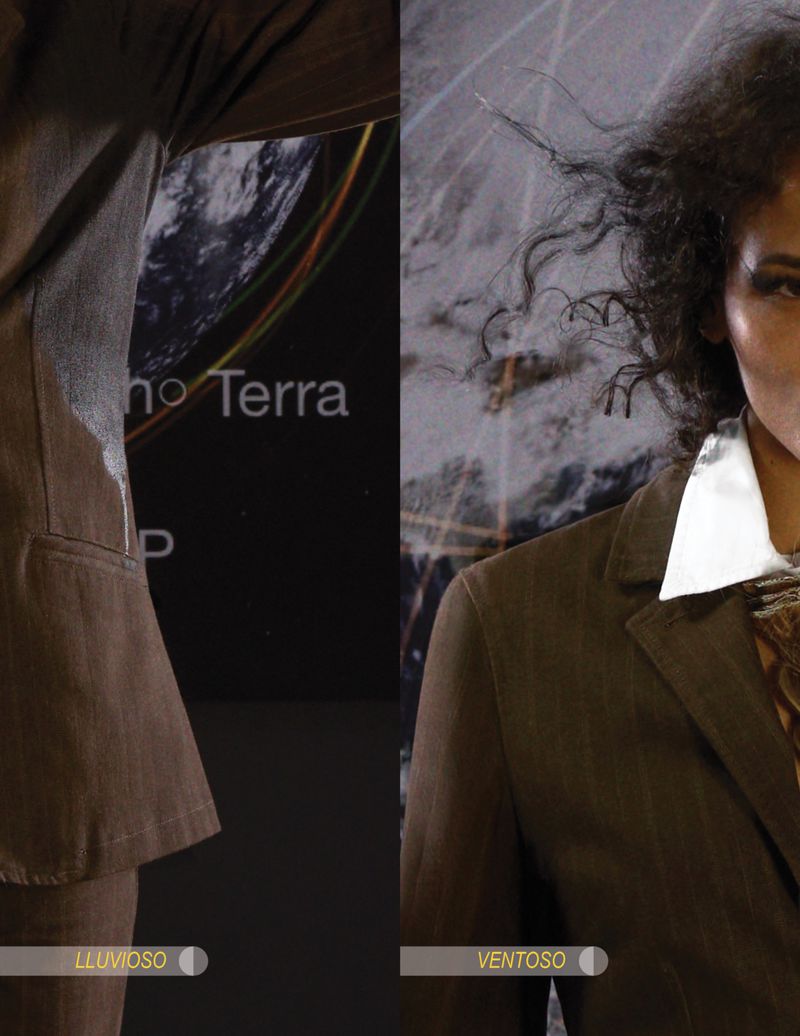 Woman in brown suit with wind-blown hair poses indoors against backdrop with globe image and text, showcasing fashion and style.