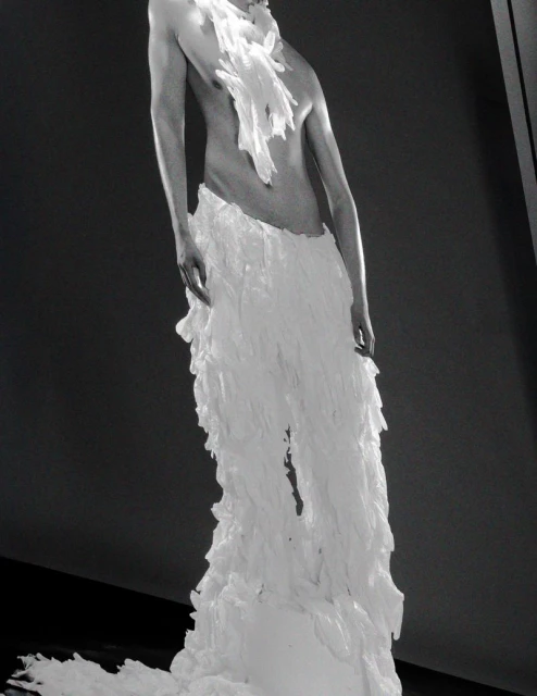 Fashion editorial featuring an adult model in a avant-garde white frilled costume against a dark gray background in an indoor setting.