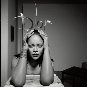 Rihanna resting her head in her hands wearing a sculptural metallic Dior tiara in a black and white studio portrait.