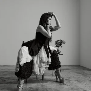 Rihanna posing in a black satin top, tiered lace skirt, and textured trousers in a black and white studio portrait.
