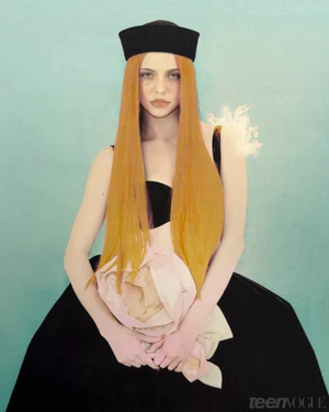 Adéla Jergová wearing a black sailor hat, black gown, and long straight orange hair against a teal background for Teen Vogue.