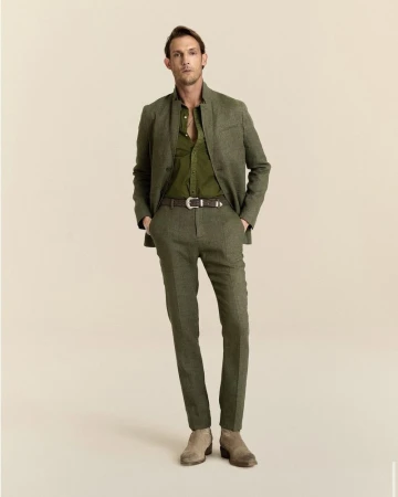 Pawel Binczak wearing an olive green suit with a stand collar jacket and suede boots against a beige studio backdrop.