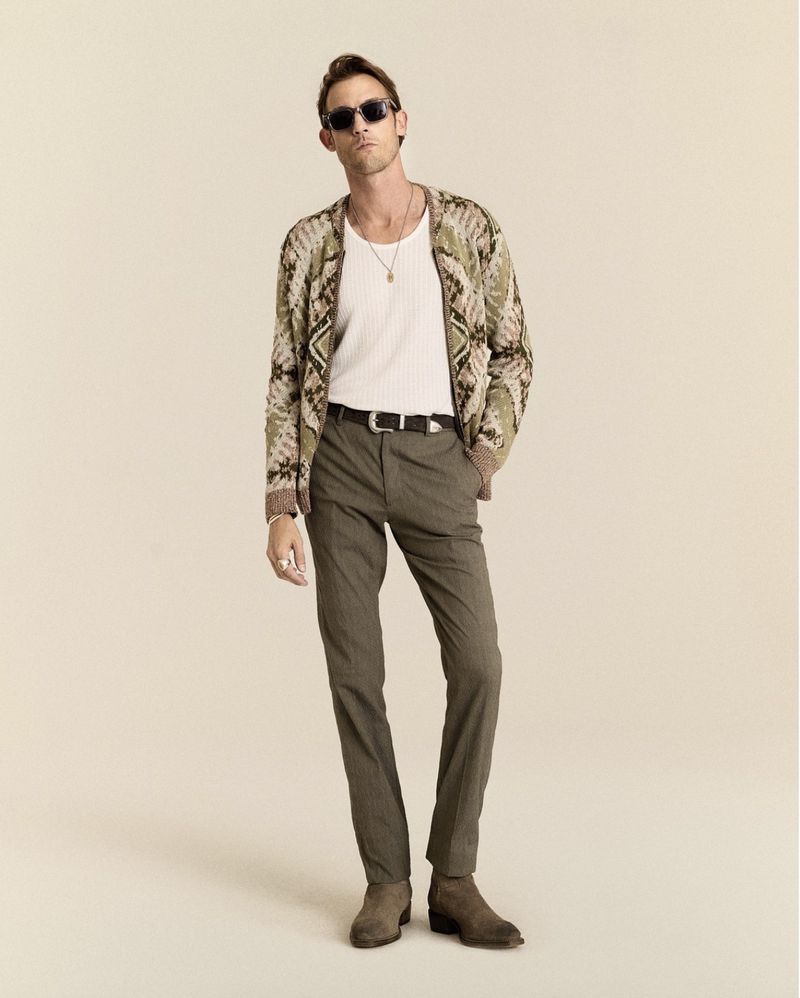 Model Pawel Binczak wearing a patterned knit cardigan, white tank top, tailored trousers, and sunglasses against a beige backdrop.