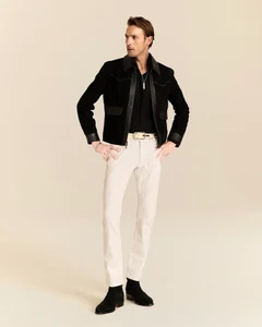 Pawel Binczak wearing a black leather-trimmed jacket, cream trousers, and black boots for John Varvatos against a warm studio backdrop.