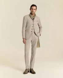 Model Pawel Binczak wearing a beige high-collar tailored suit, patterned scarf, and boots against a cream studio backdrop.