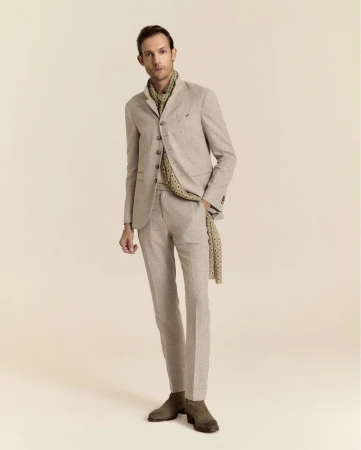 Model wearing a tailored beige stand-collar suit, patterned scarf, and suede boots against a warm plain studio backdrop.