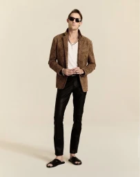 Model Pawel Binczak wearing a brown textured jacket, white top, black trousers, and sunglasses on a beige background.