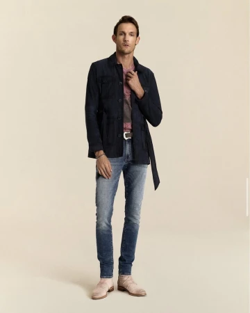 Model Pawel Binczak wearing a dark navy belted jacket, blue jeans, and light tan boots against a warm neutral studio backdrop.