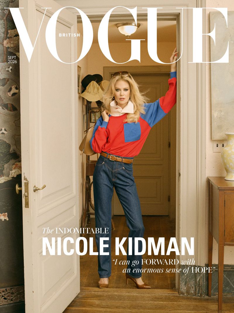 Nicole Kidman on the cover of British Vogue, wearing a red and blue long-sleeved top and dark blue jeans, standing in a doorway.
