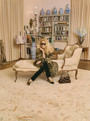 Nicole Kidman wearing sunglasses and a leopard print coat seated on an antique chaise lounge in a library room.