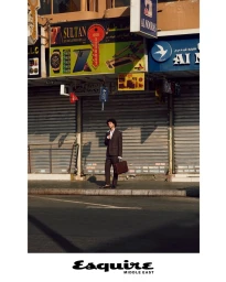 Model Leo Comanescu holding a leather briefcase on a city sidewalk in front of closed shop shutters for Esquire Middle East.