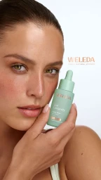 Model Emma Todt holds a mint green Weleda serum bottle next to her face against a pure white studio background.
