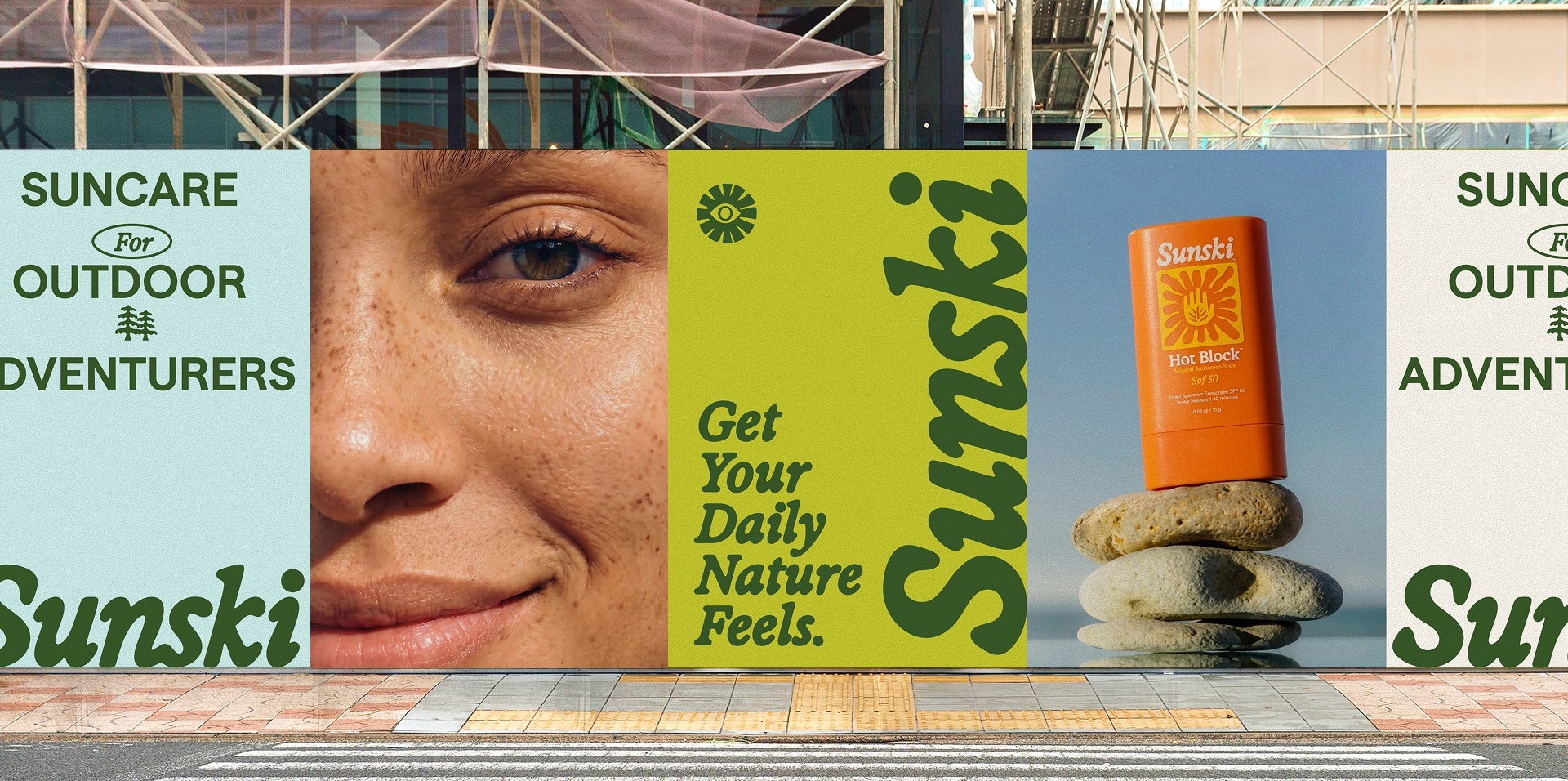 Outdoor billboard campaign for Sunski featuring suncare branding, a close-up freckled face, and an orange sunscreen stick on stacked stones.