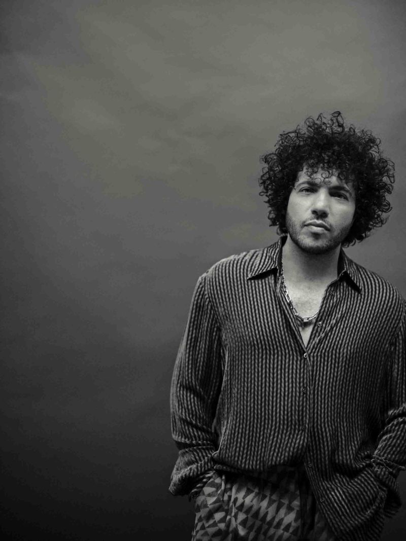 Benny Blanco in a striped button-up shirt and chain necklace posing against a dark grey studio backdrop in black and white.