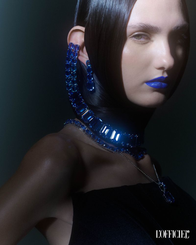 Close-up beauty shot of a fair-skinned woman with sleek black hair, dramatic blue lipstick, and matching blue gemstone jewelry.