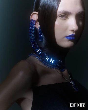 Close-up beauty shot of a fair-skinned woman with sleek black hair, dramatic blue lipstick, and matching blue gemstone jewelry.