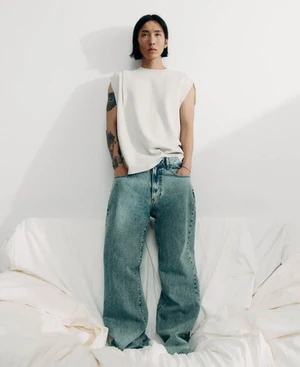 Model Hyuk Kim posing in a white sleeveless top and wide-leg denim jeans against a white backdrop for Adolfo Dominguez.