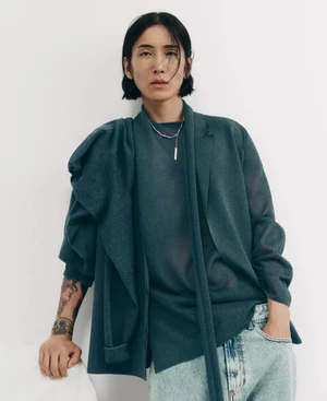 Model Hyuk Kim posing in a dark teal draped jacket, matching shirt, and light wash denim against a white studio background.