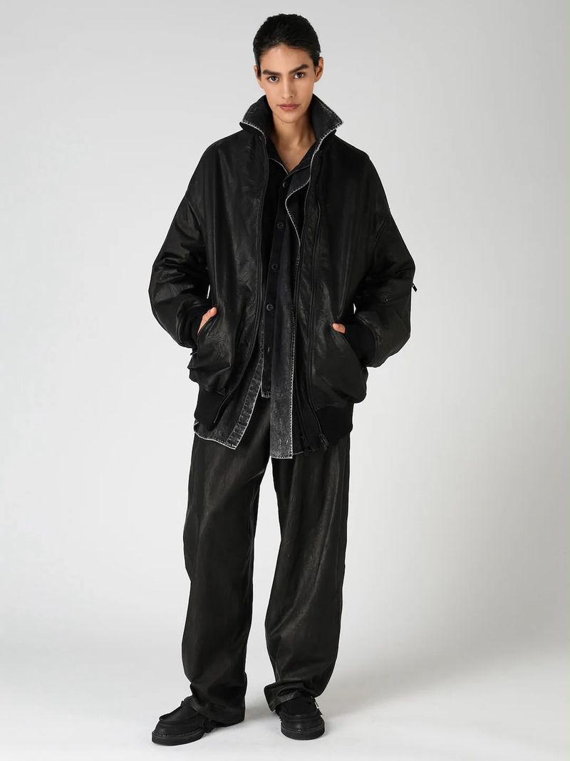 Model Katterine Anzures wears an oversized black jacket and matching wide-leg trousers against a light grey studio background.