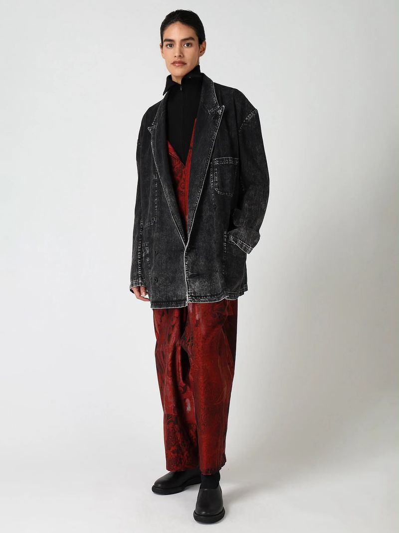 Model Katterine Anzures in an oversized washed black denim blazer and red printed trousers against a white studio background.