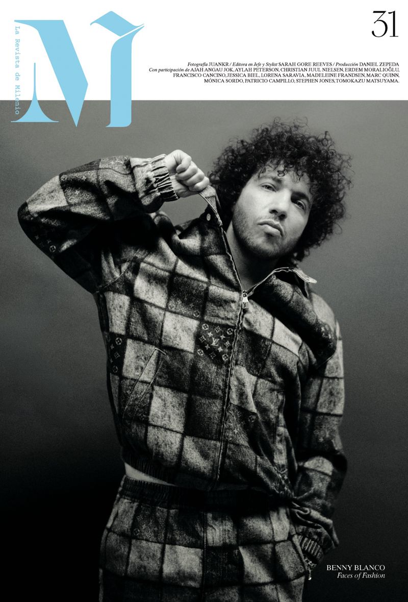 Portrait of Benny Blanco with curly hair wearing a dark patterned checkerboard zip-up jacket against a plain grey backdrop.