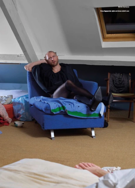 Person sitting in a blue chair, wearing a black dress and pantyhose. The setting is indoors in a room with white walls and a sloped ceiling.