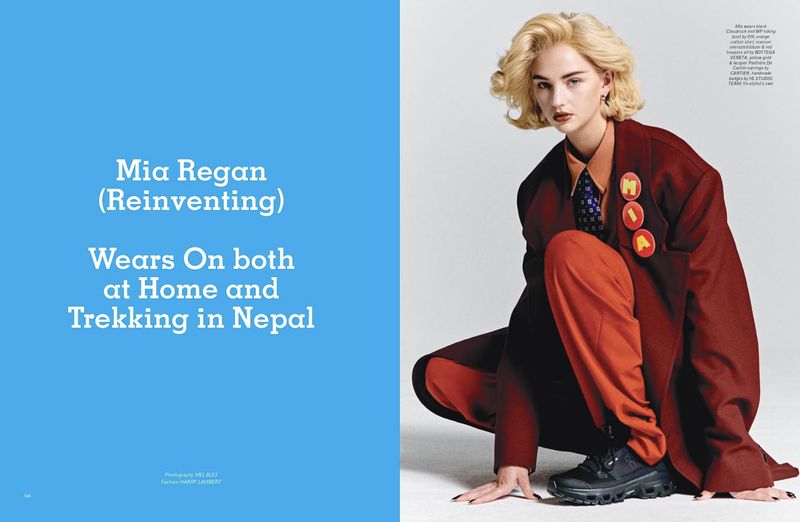 Fashion editorial shot of a blonde woman in a red blazer and pants, posing in a studio against a white backdrop. Style and beauty focus.