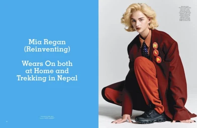 Model Mia Regan crouching in an oversized burgundy coat and orange trousers against a studio background beside blue editorial text.