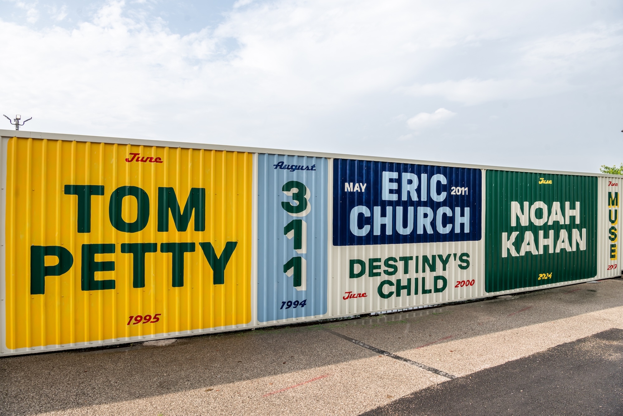 Live Nation branded metal shipping container wall featuring graphic festival style concert posters for various musical artists.