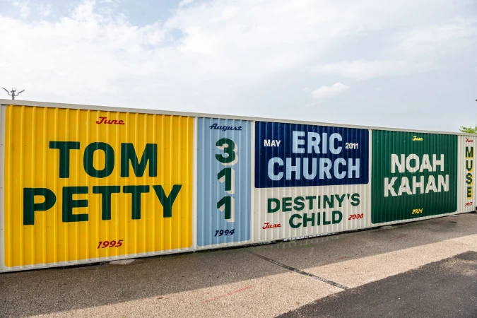 Live Nation branded metal shipping container wall featuring graphic festival style concert posters for various musical artists.
