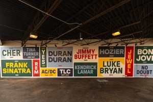 Painted wall mural featuring bold typography of famous concert artists and performance dates beneath an industrial open ceiling.