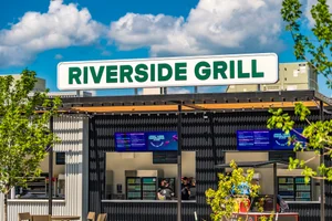 Exterior of Riverside Grill food kiosk with modern black corrugated siding under a blue sky with clouds.