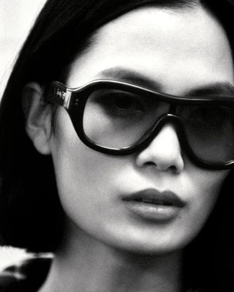 Black and white close-up portrait of model Haojie Qi wearing oversized dark sunglasses with thick black frames.